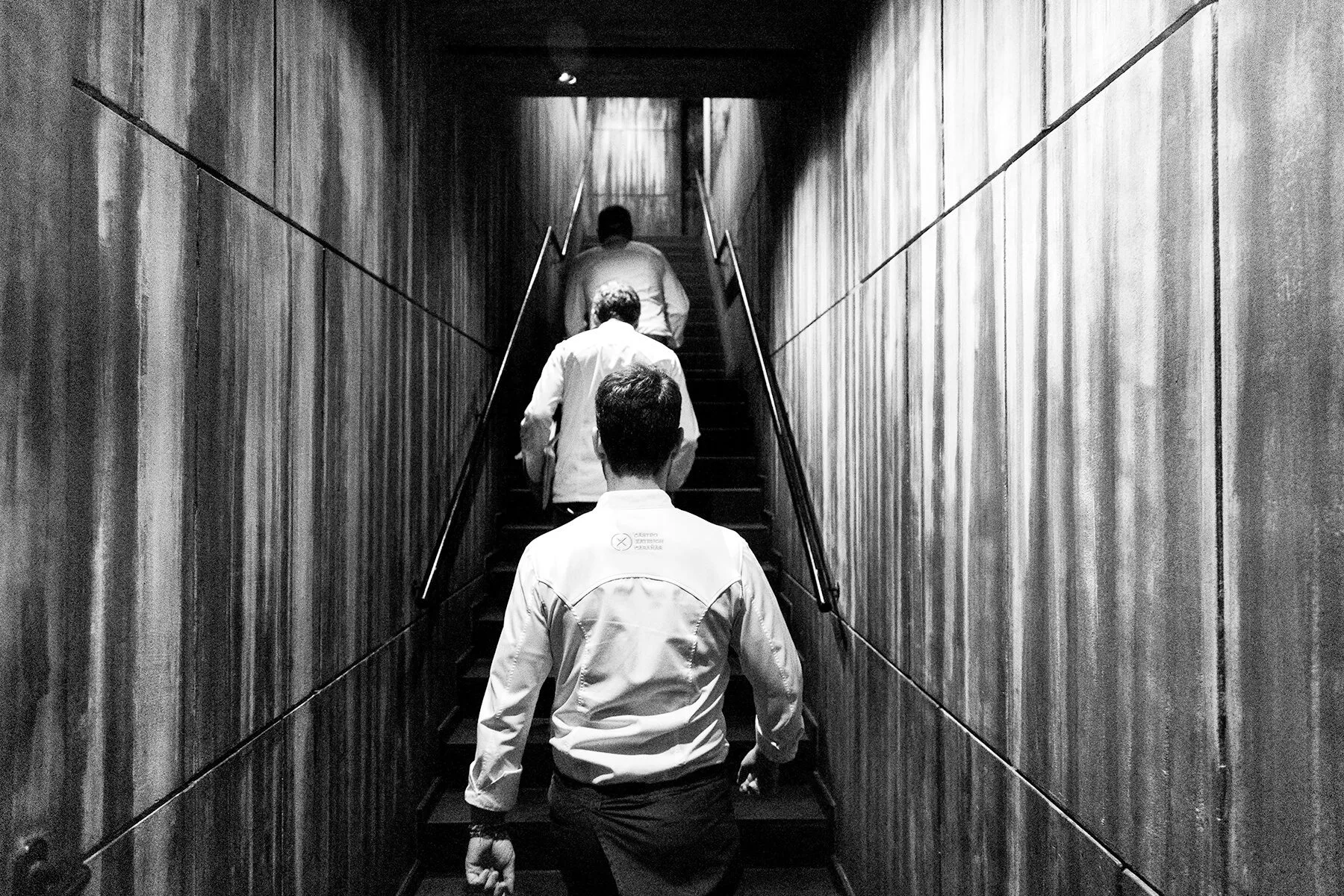 Tres camareros subiendo las escaleras en el restaurante Disfrutar de Barcelona, en fotografía en blanco y negro.
