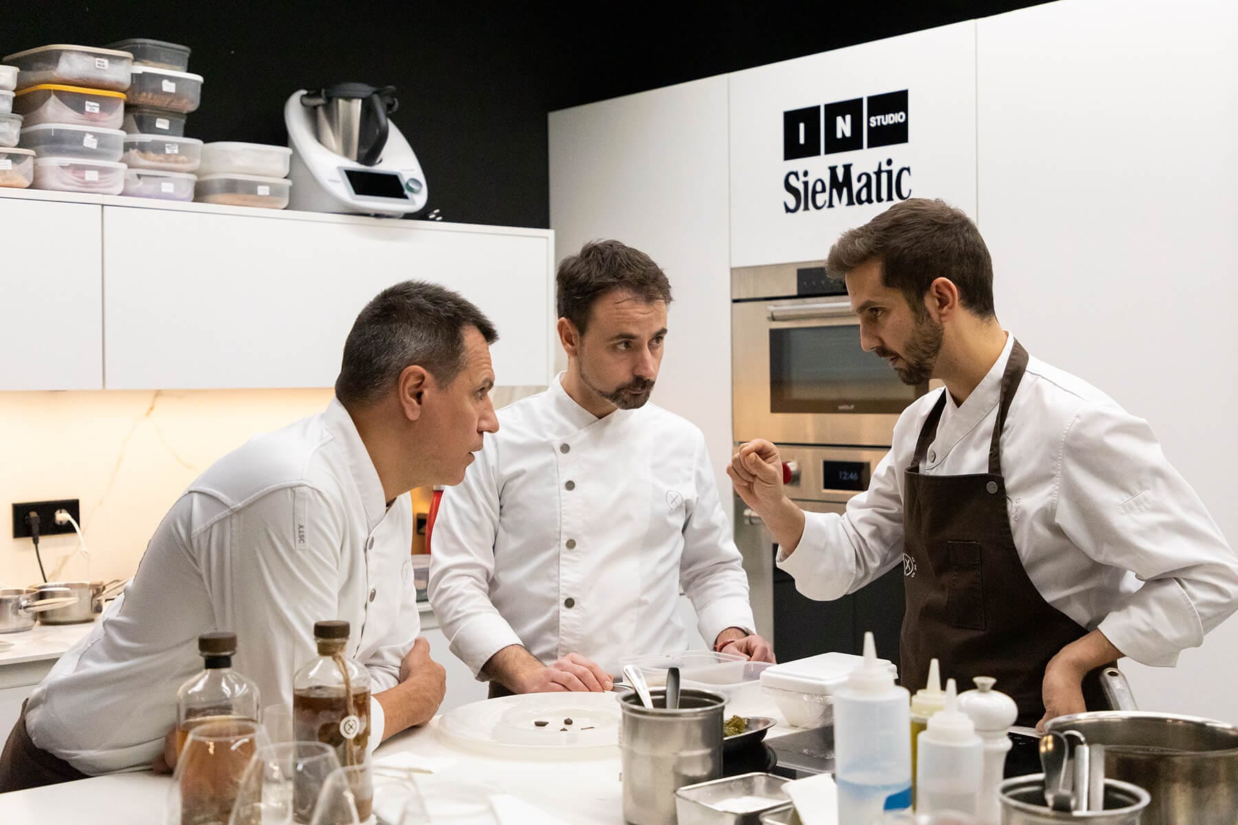 Tres chefs reunidos conversando en la cocina del restaurante Disfrutar en Barcelona, mostrando trabajo en equipo y creatividad gastronómica.