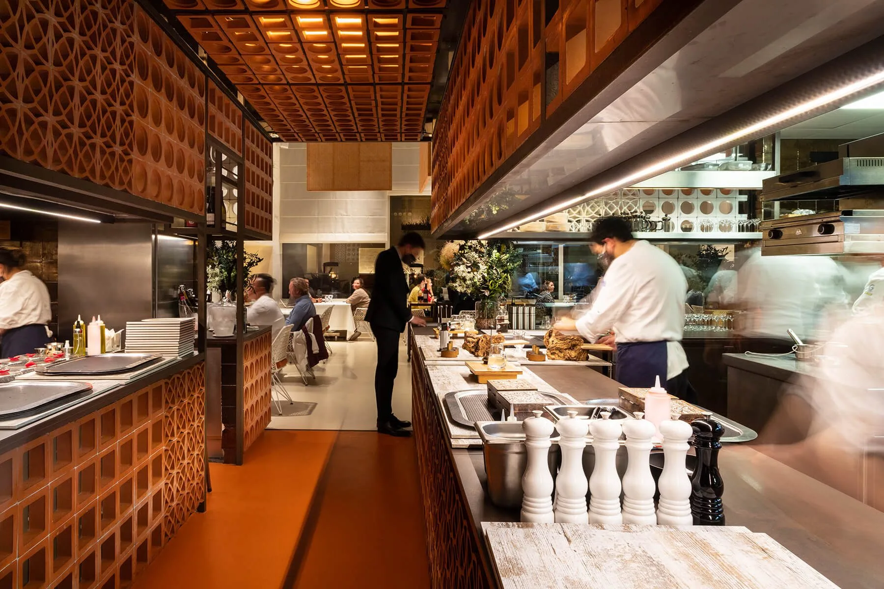 Cocina abierta en el restaurante Disfrutar de Barcelona con chefs trabajando y clientes comiendo al fondo.