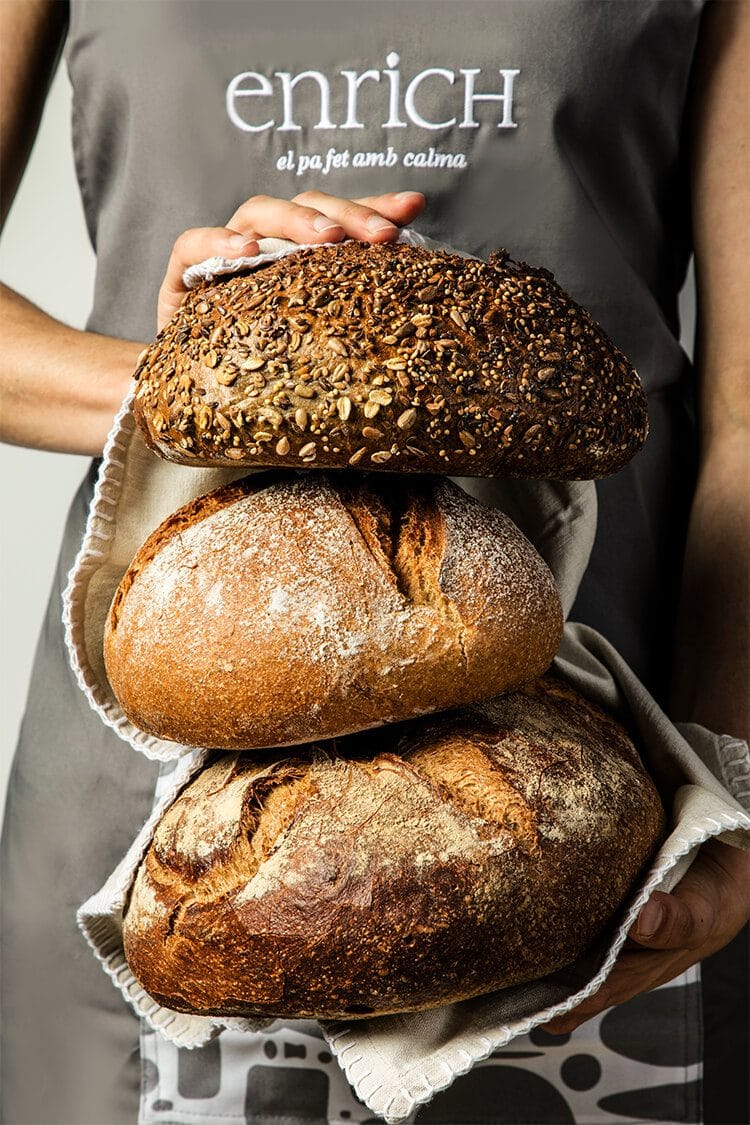 Fotografía de producto con panes de pagés sostenidos por dependienta de Panadería Enrich en Barcelona. Fotógrafo profesional de productos en España.