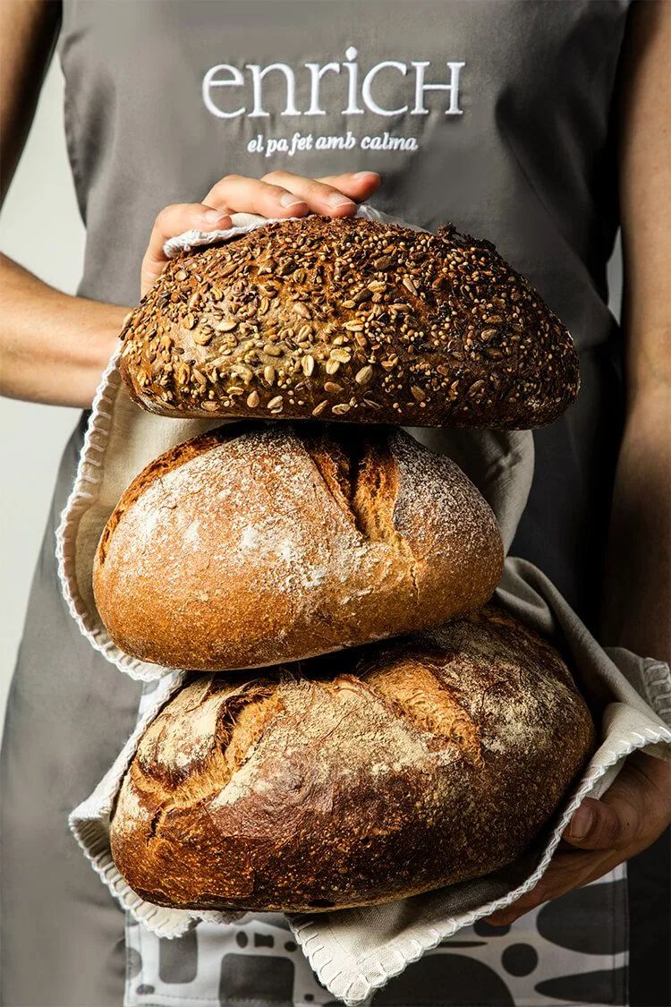 Fotografía de producto con panes de pagés sostenidos por dependienta de Panadería Enrich en Barcelona. Fotógrafo profesional de productos en España.