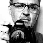 Autorretrato de fotógrafo profesional en España, en blanco y negro frente al espejo, mostrando su rostro y cámara, con estilo de auto-retrato.