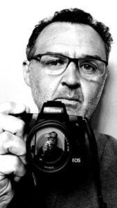 Autorretrato de fotógrafo profesional en España, en blanco y negro frente al espejo, mostrando su rostro y cámara, con estilo de auto-retrato.