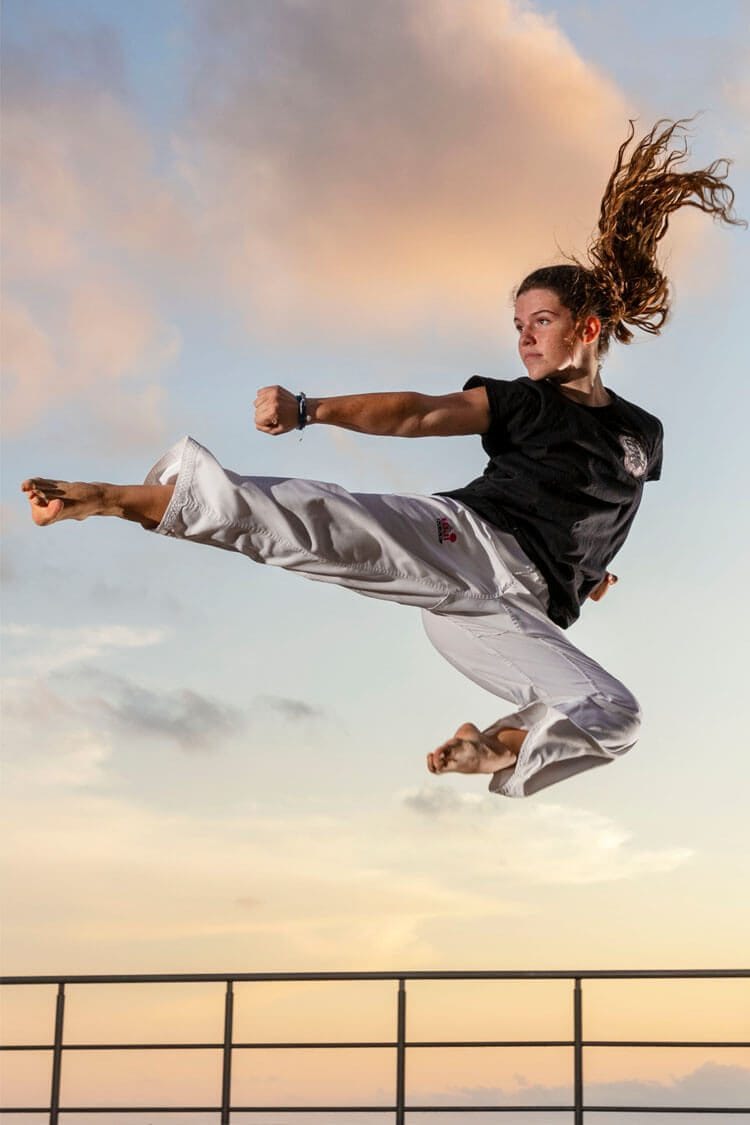 Retrato deportivo profesional de Valeria en el aire haciendo una postura de taekwondo, fondo cielo azul, fotografía en Barcelona.