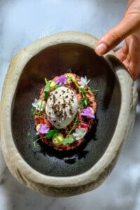 Postre creativo de arroz dulce con frutas de verano, helado de vainilla y flores comestibles, servido en bol de piedra en Casa Varela Barcelona, fotografía gastronómica profesional.