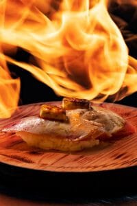 Nigiris de atún con foie sobre tabla de madera siendo flambeados, con llamas iluminando la escena en Sushi Kurama, fotógrafo profesional en Barcelona.
