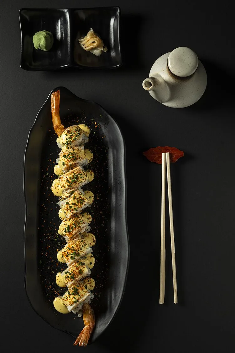 Uramaki de tempura de langostino con decoración gourmet, acompañado de palillos, wasabi, jengibre y salsa de soja en Bodegón Sushi Kurama, fotógrafo profesional en Barcelona.