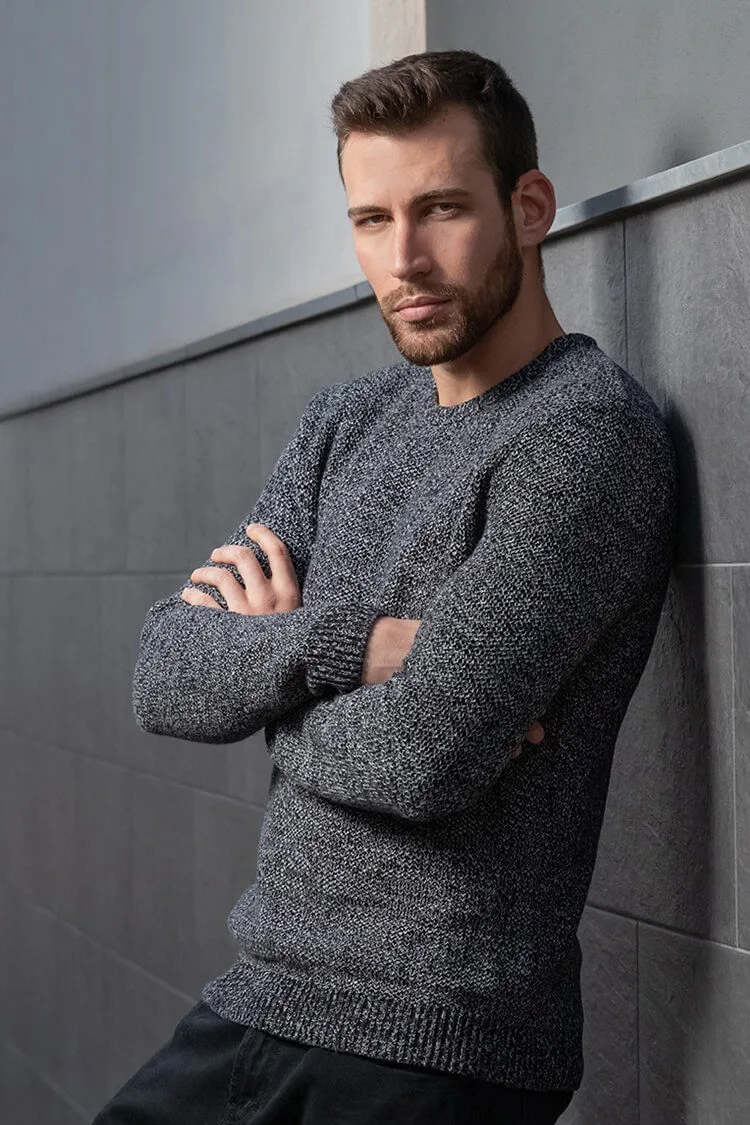 Retrato de Jadier con sonrisa sensual, brazos cruzados y apoyado en la pared en una pose informal y moderna.