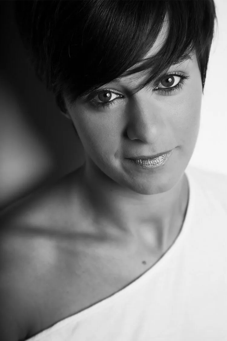 Retrato profesional en blanco y negro de Marta, en Barcelona, sonriendo con sinceridad a cámara, con el hombro descubierto y un peinado elegante.