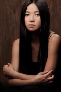 Retrato profesional de una chica asiática encogida que transmite fragilidad y timidez, estilo artístico en blanco y negro.