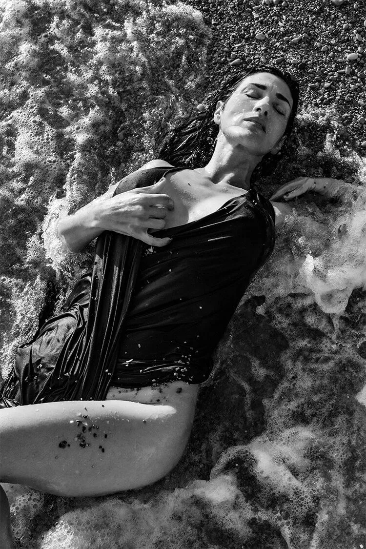 Retrato artístico en blanco y negro de Tamara estirada sensualmente en el agua en la orilla de la playa de Valencia.