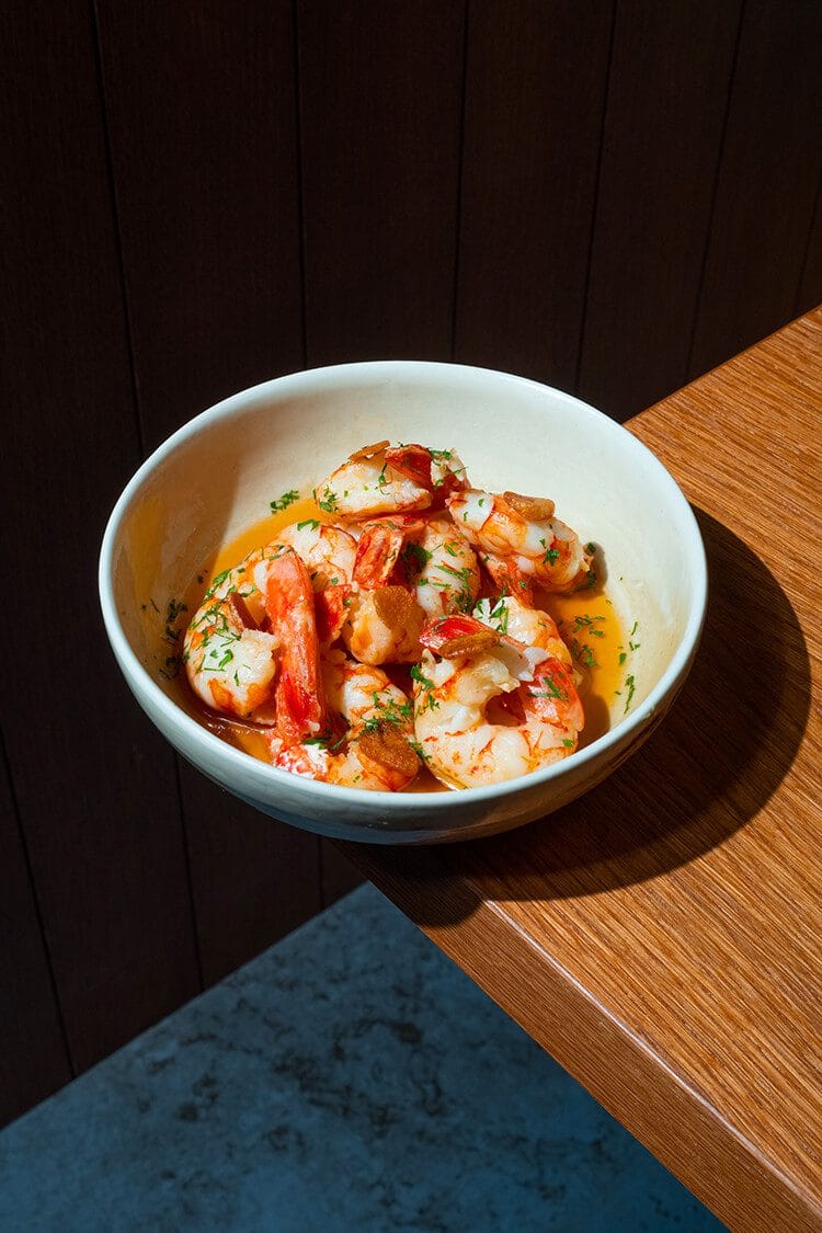 Gambas al ajillo con perejil servidas en plano estético en la punta de una mesa en el restaurante Txapela de Madrid.
