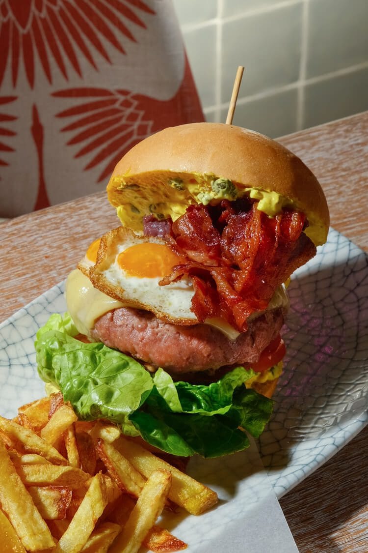 Hamburguesa completa de ternera con lechuga, queso, huevo y bacon, acompañada de patatas, servida en plato sobre mesa. Restaurante Big, fotógrafo profesional en Madrid.