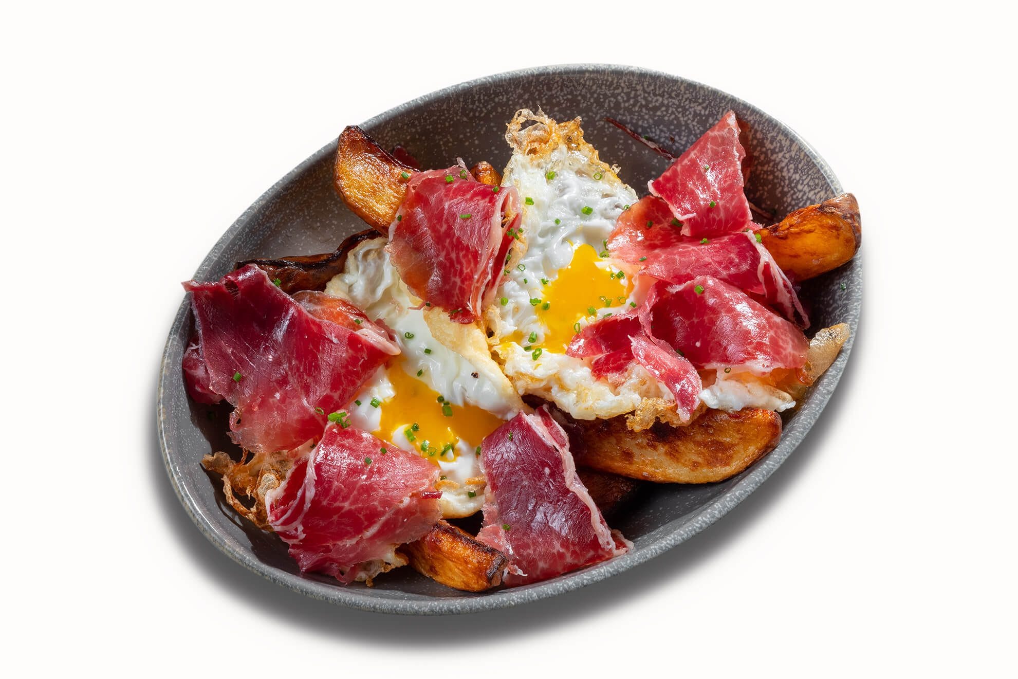 Huevos rotos con jamón serrano sobre patatas fritas, plato típico español en el restaurante Txapela de Madrid, fotografía profesional.
