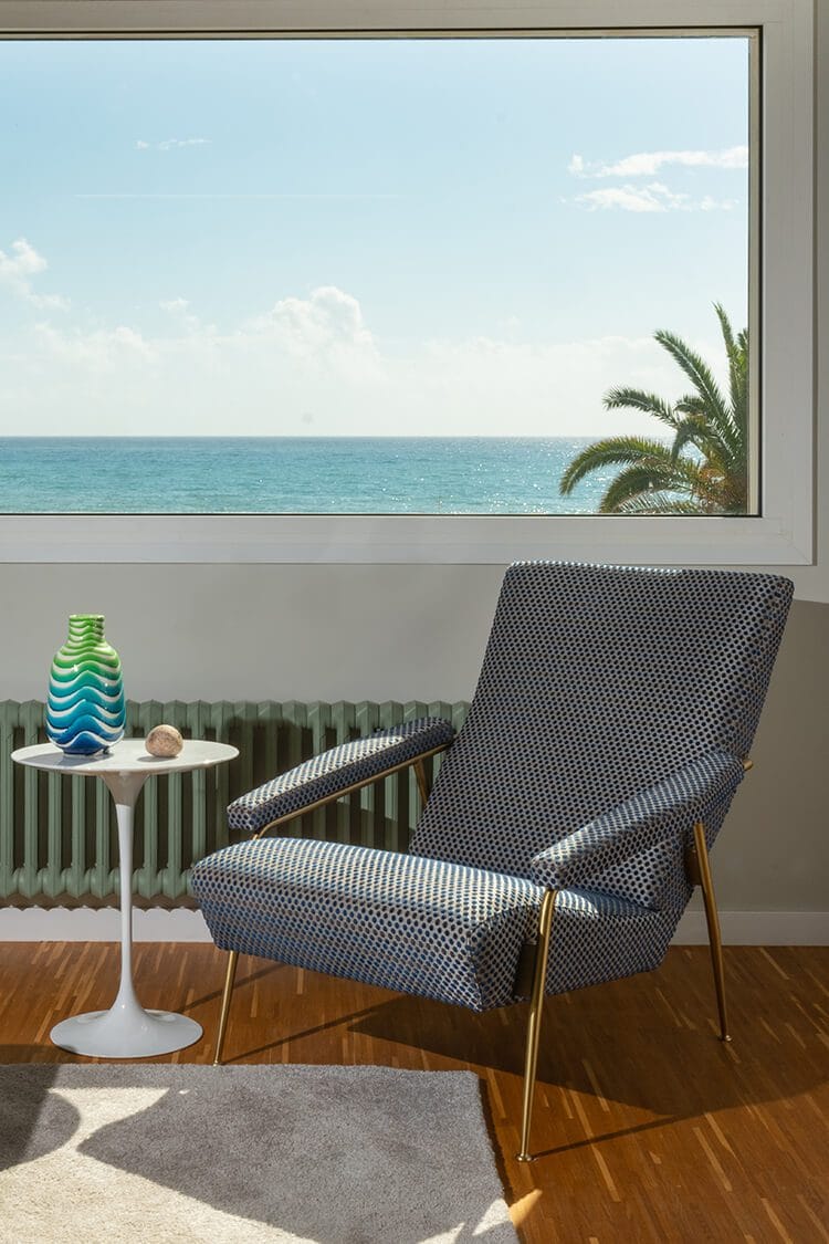 Fotografía de interior en hotel Nunue con sillón, ventana grande y vistas al mar en Barcelona