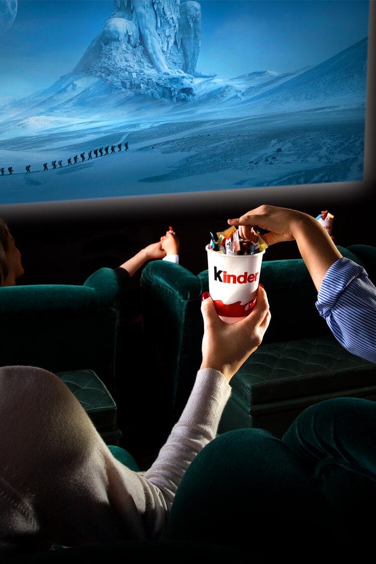 Fotografía de una pareja disfrutando mini chocolates Kinder en el cine, con película de fondo y vaso promocional. Fotógrafo profesional de productos en España.