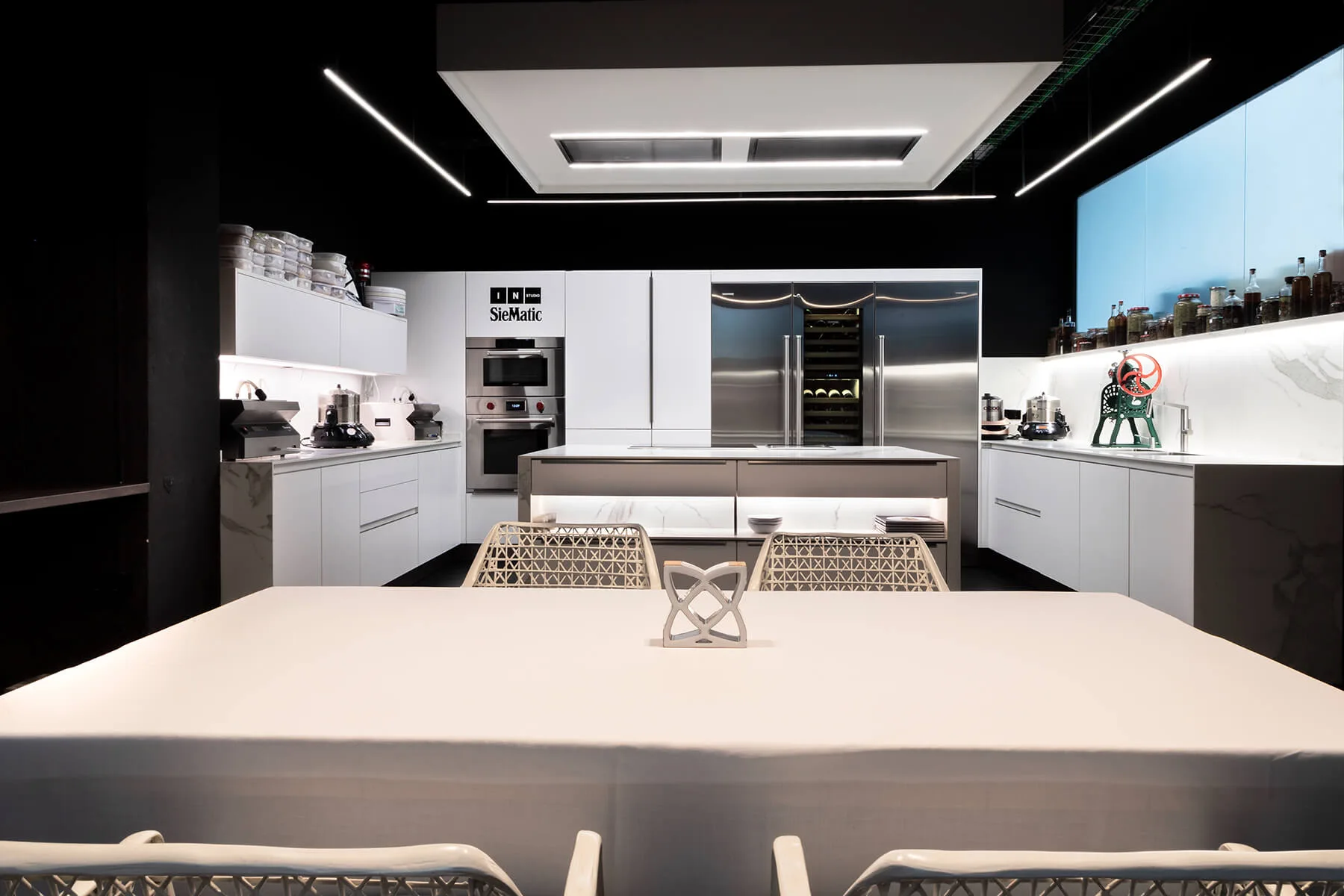 Mesa de comedor elegante en primer plano con cocina apaisada blanca y negra al fondo, en restaurante Disfrutar, Barcelona, ambiente luminoso y sofisticado.