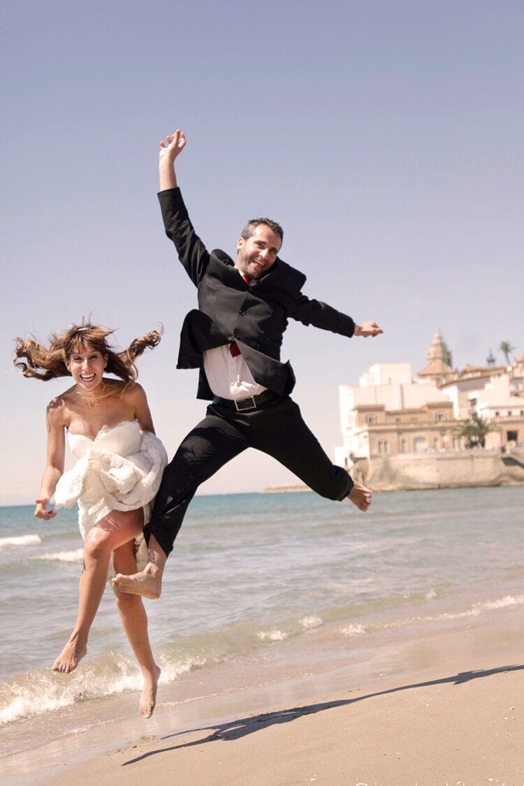 Pareja casada saltando y riendo en la orilla de la playa en Barcelona