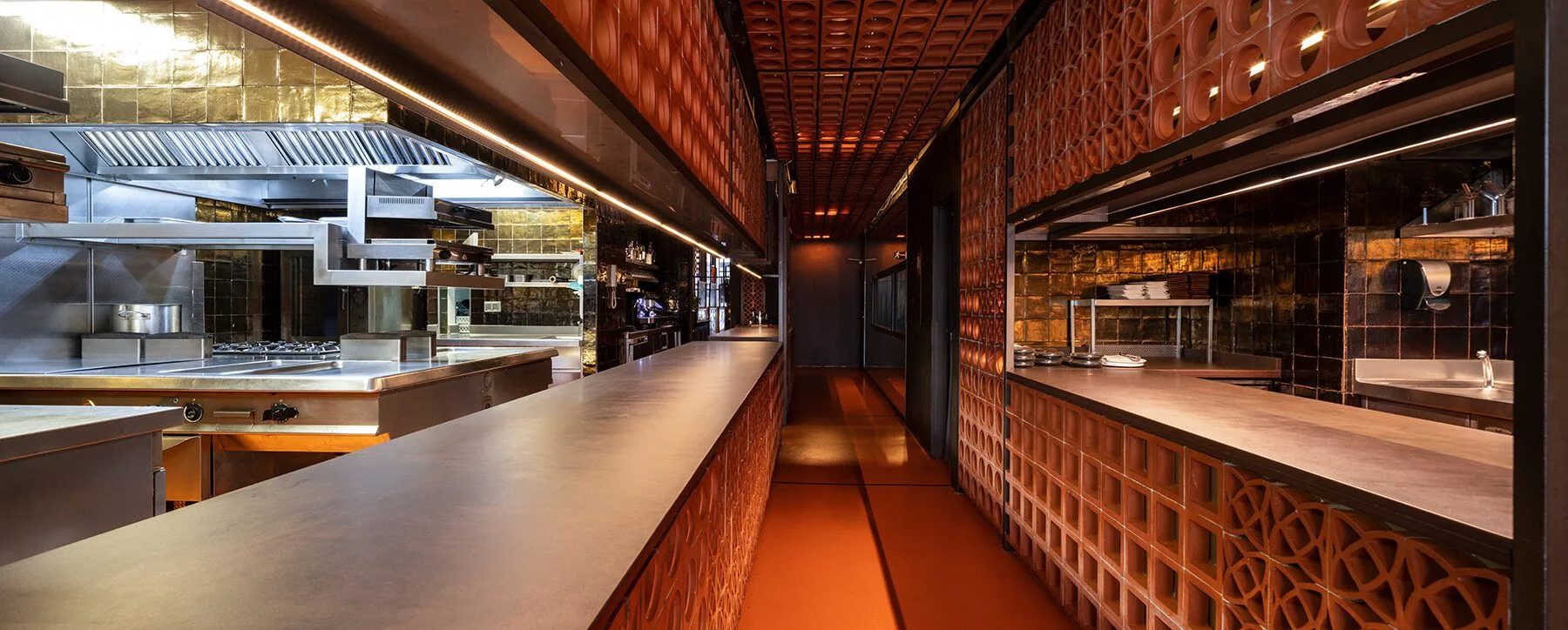 Pasillo central con cocinas a ambos lados en el restaurante Disfrutar de Barcelona, destacando la iluminación moderna. Fotógrafo profesional gastronómico.