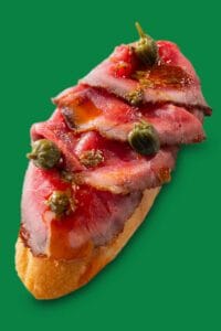 Tapa española de ternera sobre pan con decoración gourmet, fotografía profesional en restaurante Txapela de Madrid.