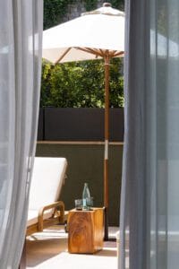 Fotografía profesional de la terraza de una habitación del Hotel Miramar en Barcelona con sombrilla blanca, hamaca y bebidas bajo el sol