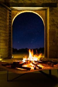 Torreón de piedra con portón de hierro abierto y hoguera encendida bajo cielo nocturno en Teruel