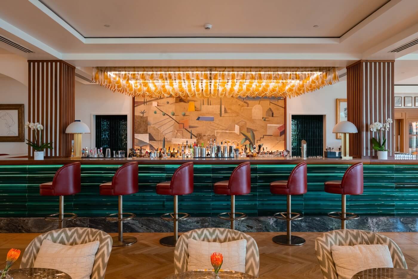Barra del bar del hotel St. Regis en Madrid con taburetes rojos, iluminación elegante y decoración artística