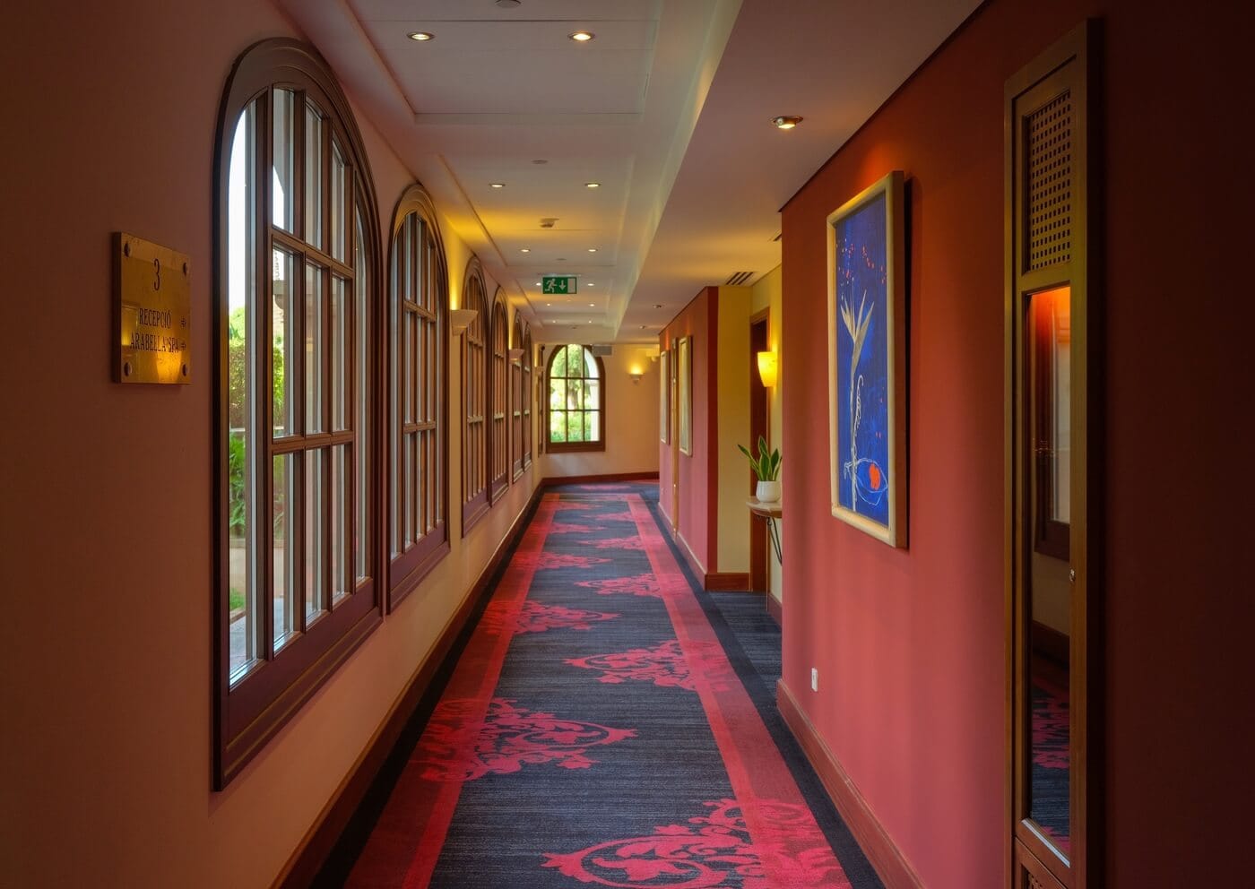 Pasillo elegante del hotel St. Regis en Mallorca con alfombra roja, ventanales clásicos y decoración artística, fotografía de interiores de hoteles profesional en España.