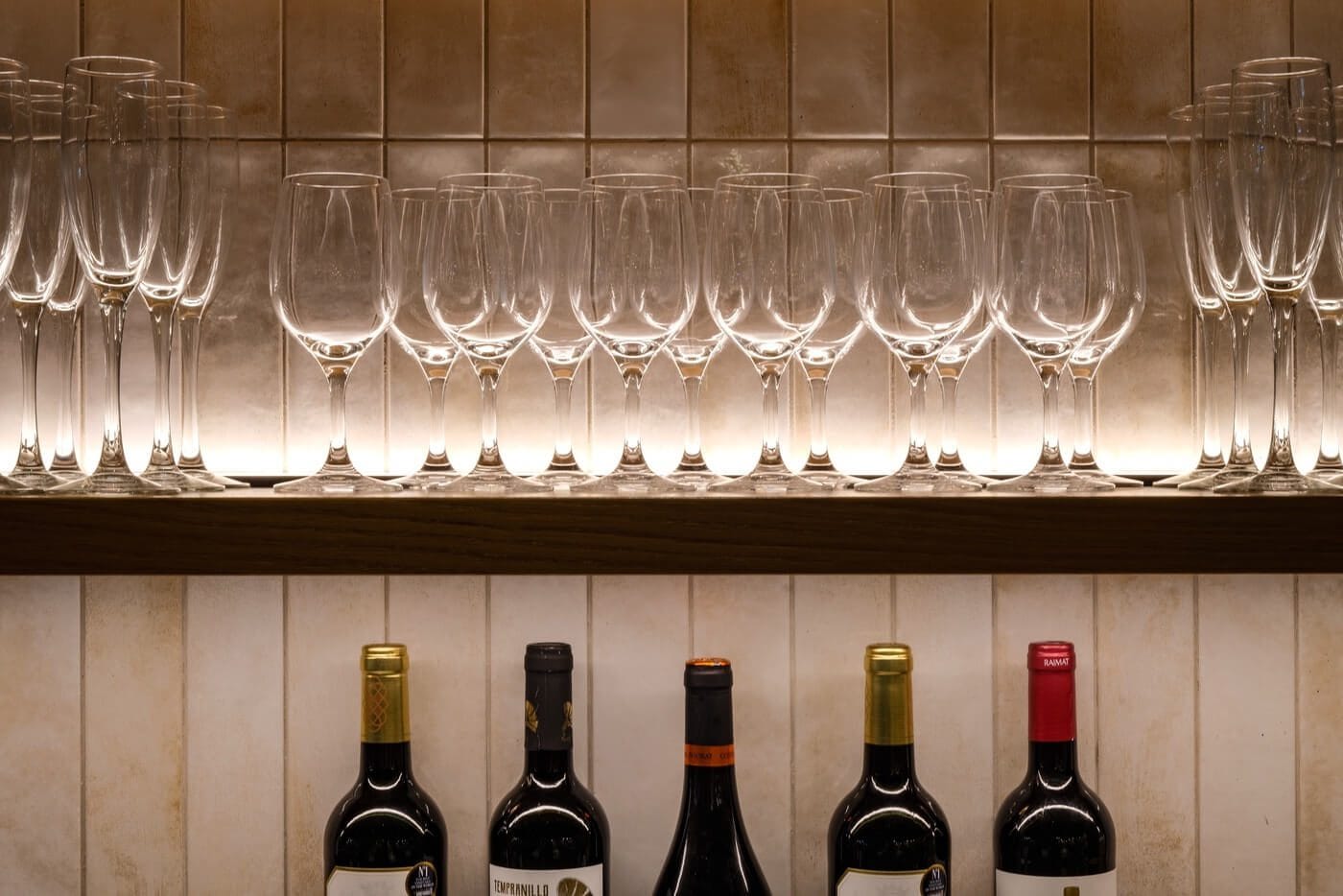 Copas de vino y cava expuestas en estantería iluminada con botellas debajo en restaurante Tapa Tapa Barcelona