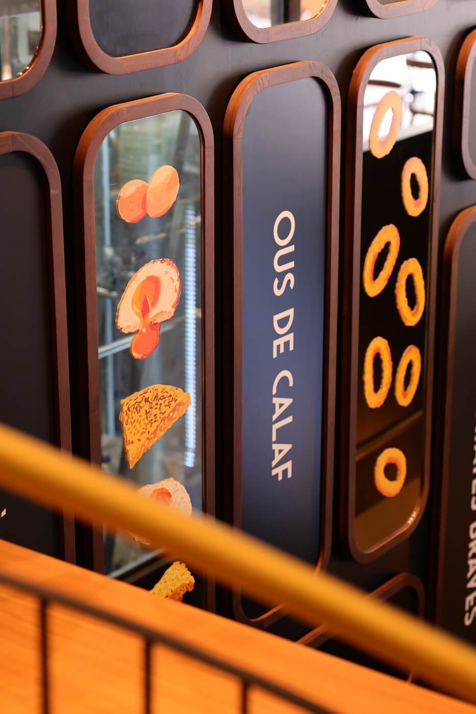 Paneles decorativos en la pared con ilustraciones de tapas y nombres como Ous de Calaf en Tapa Tapa Barcelona