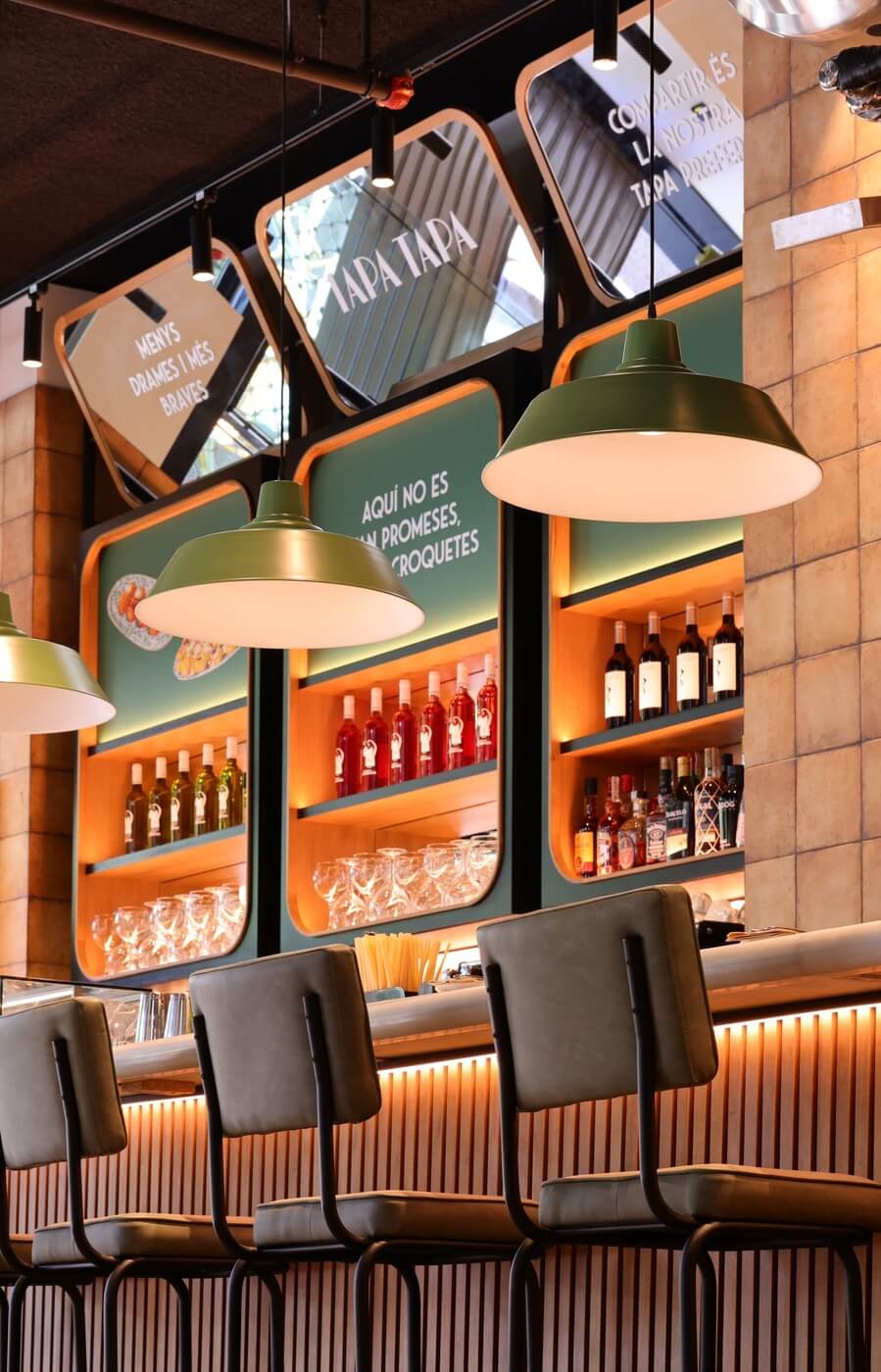 Fotografía de la barra del restaurante Tapa Tapa desde un ángulo bajo, con taburetes y estanterías de fondo.