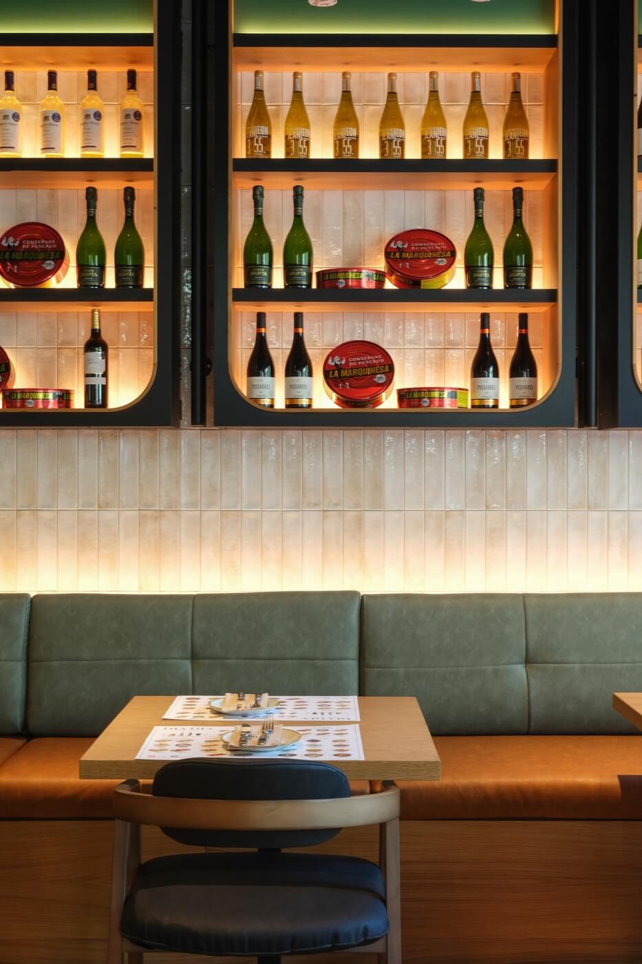 Detalle de mesa para dos con sofá y estantería de vinos en restaurante Tapa Tapa Barcelona.