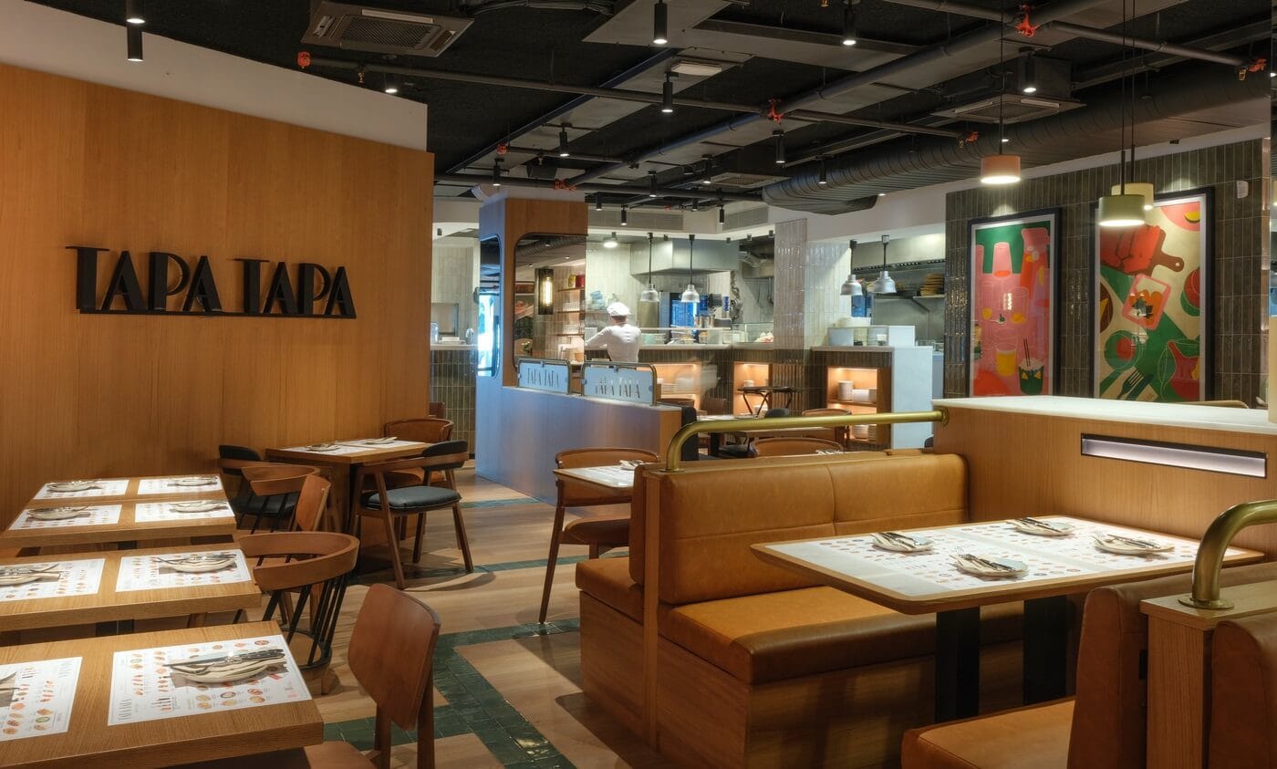 Interior del Tapa Tapa en Barcelona con cocina abierta, cuadros modernos y mesas con sofás.