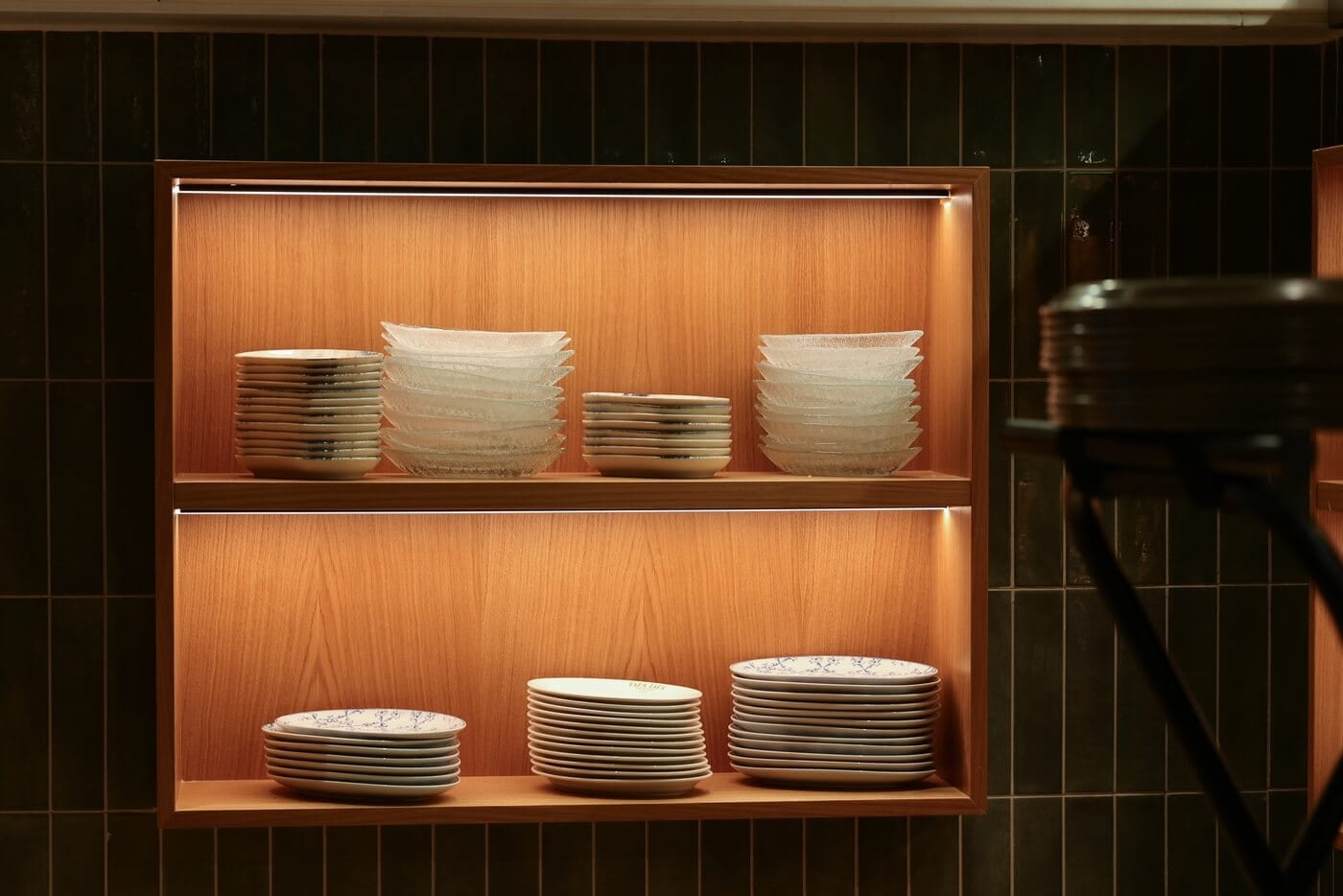 Estantería empotrada con platos expuestos para tapas sobre fondo de madera e iluminación en Tapa Tapa Barcelona