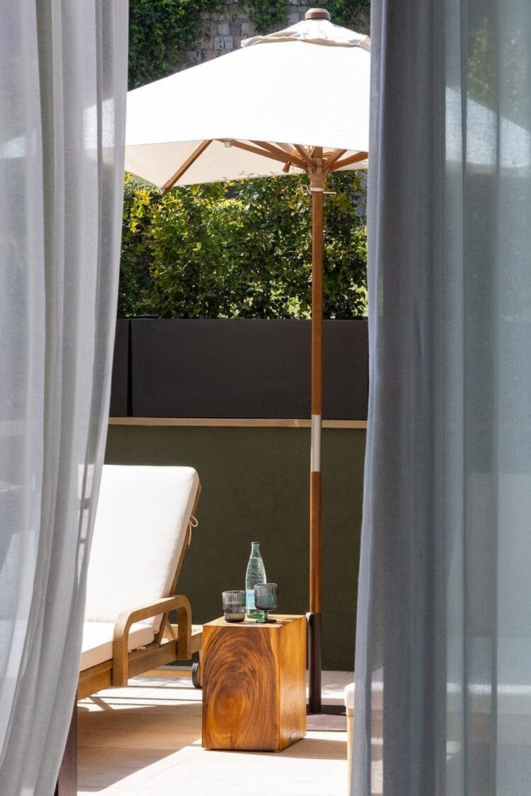 Terraza del Hotel Miramar vista entre cortinas, con tumbona, sombrilla y bebidas al sol, fotografía de interiores en Barcelona