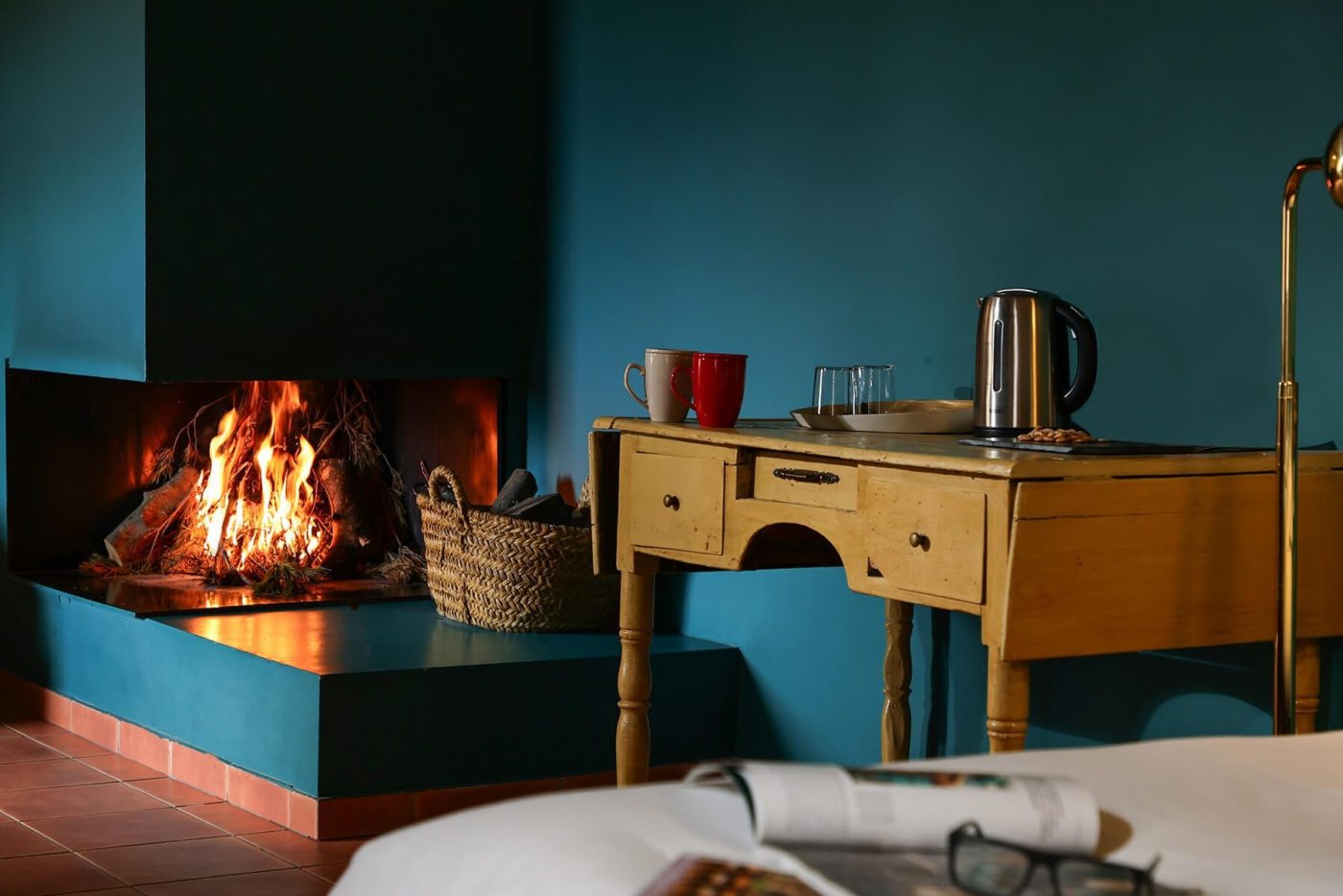 Chimenea encendida en habitación de hotel rústica con mesita y pared azul marino en Teruel