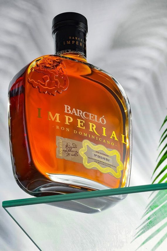 Fotografía profesional de la botella de Ron Barceló Imperial sobre mesa de cristal con fondo elegante. Fotógrafo de productos en España.
