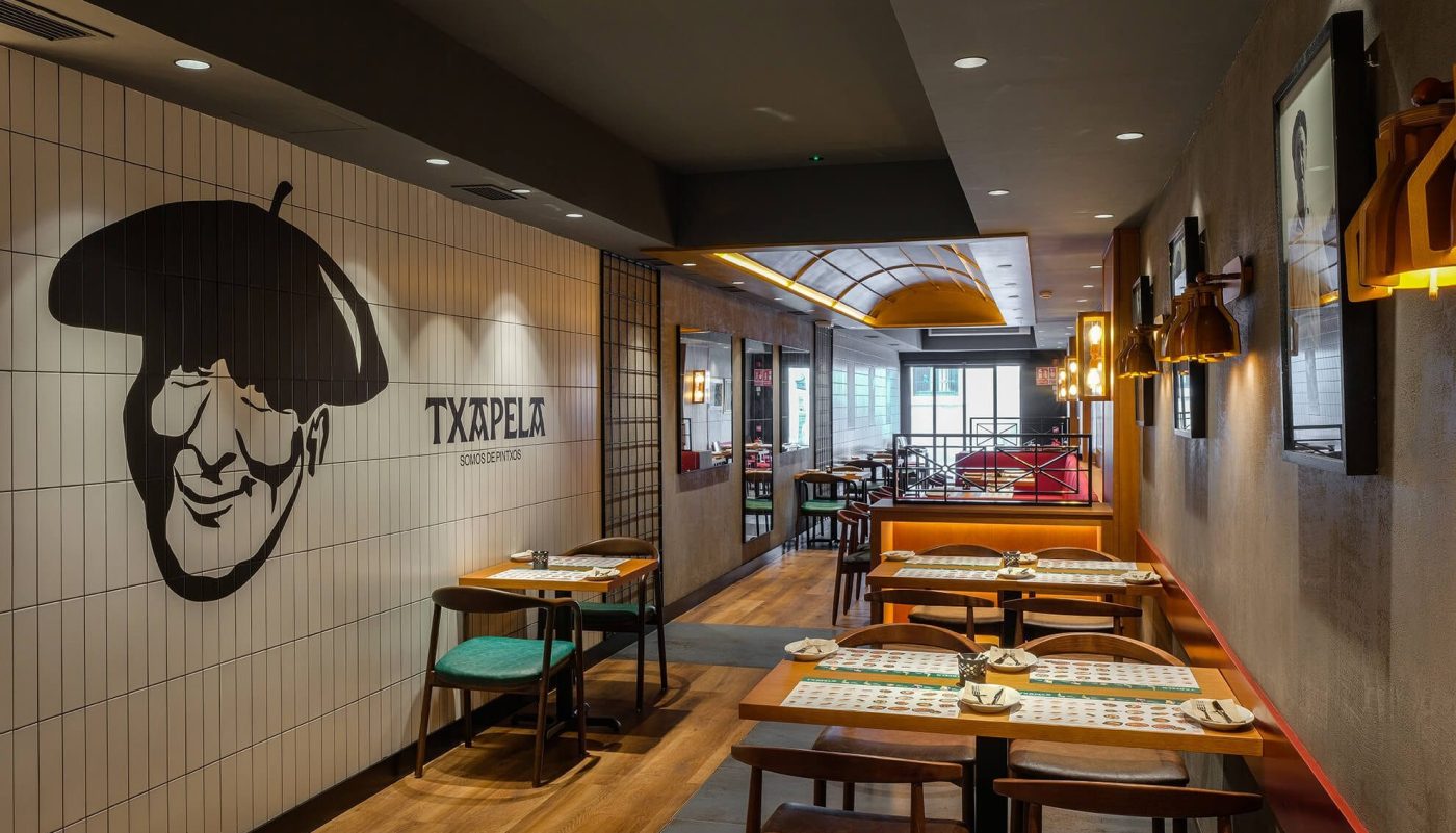 Interior elegante del restaurante Txapela en Madrid con mesas a profundidad y muro blanco minimalista, fotografía profesional.
